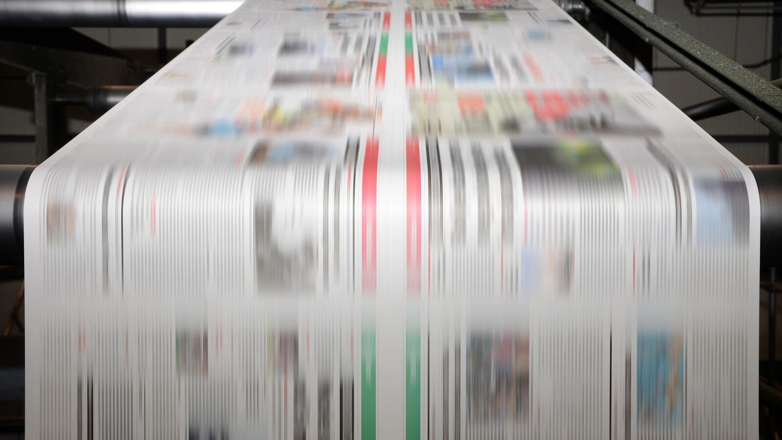 Newspaper sheets streaming through a web press at speed — color inks visible, motion-blurred copy.