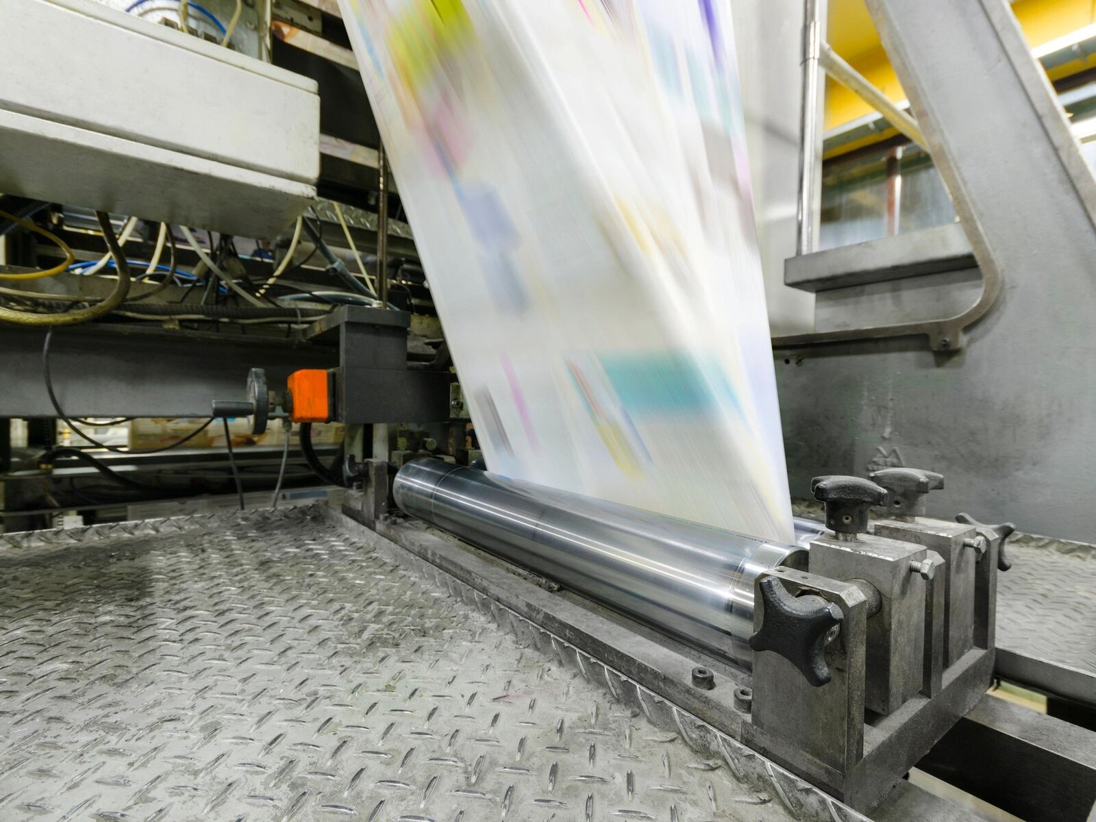 Color web press in motion — sheet running through the cylinder, multicolor inks visible mid-impression.